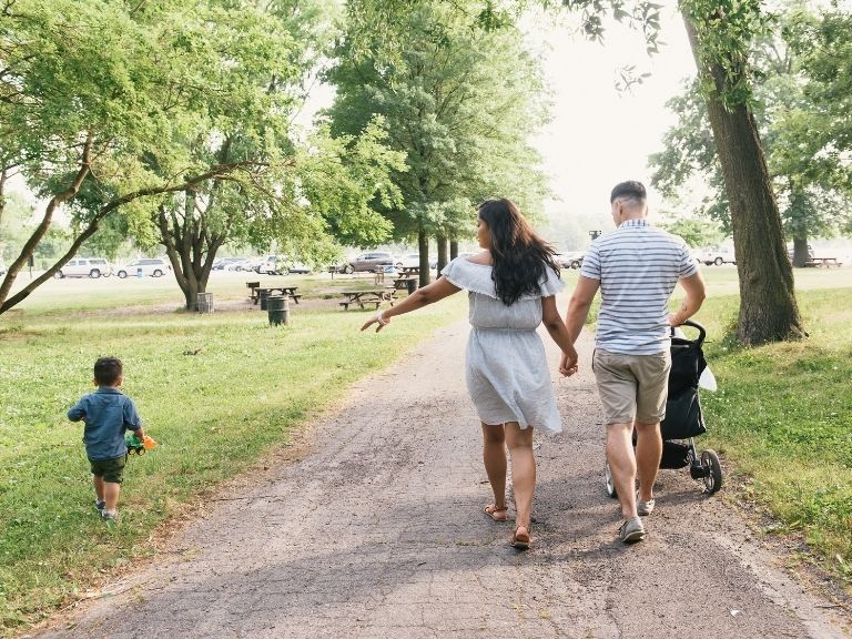 young couple pushing stroller in a park waving to little boy